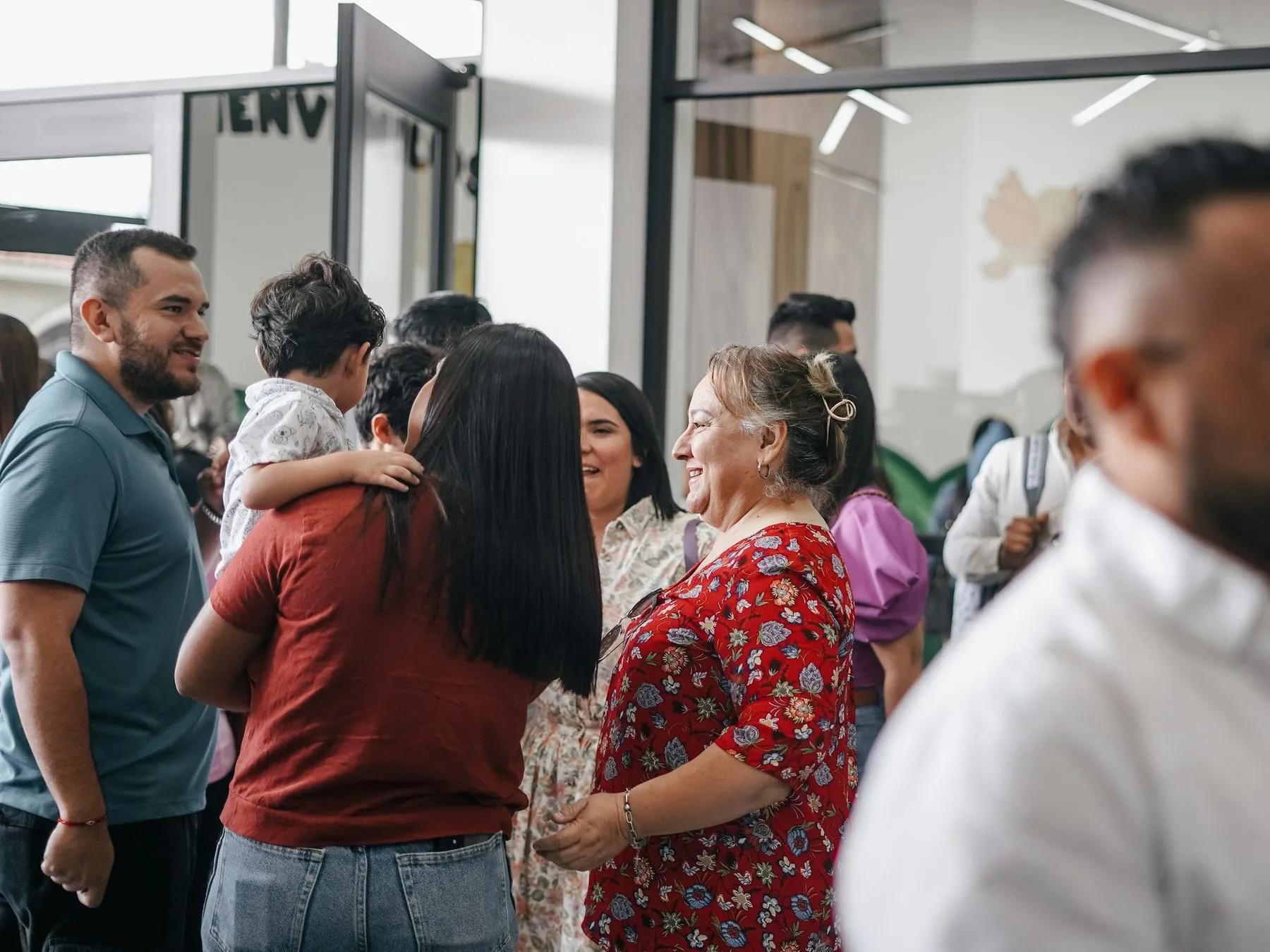 People talking in a bright church lobby on a Sunday morning, one woman holding a toddler