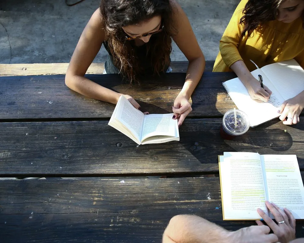 Three people reading and taking notes around a wooden picnic table